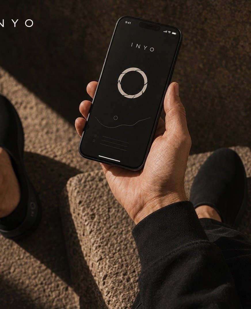 A hand holding a phone with the Inyo app open, on warm stone steps.