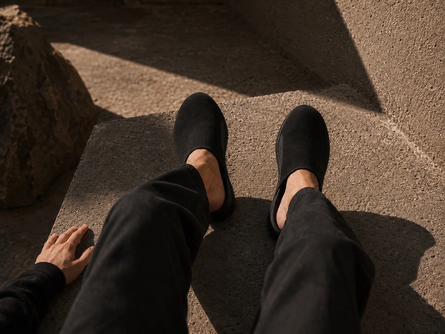 Looking down at your own feet in black mules on sunlit stone.