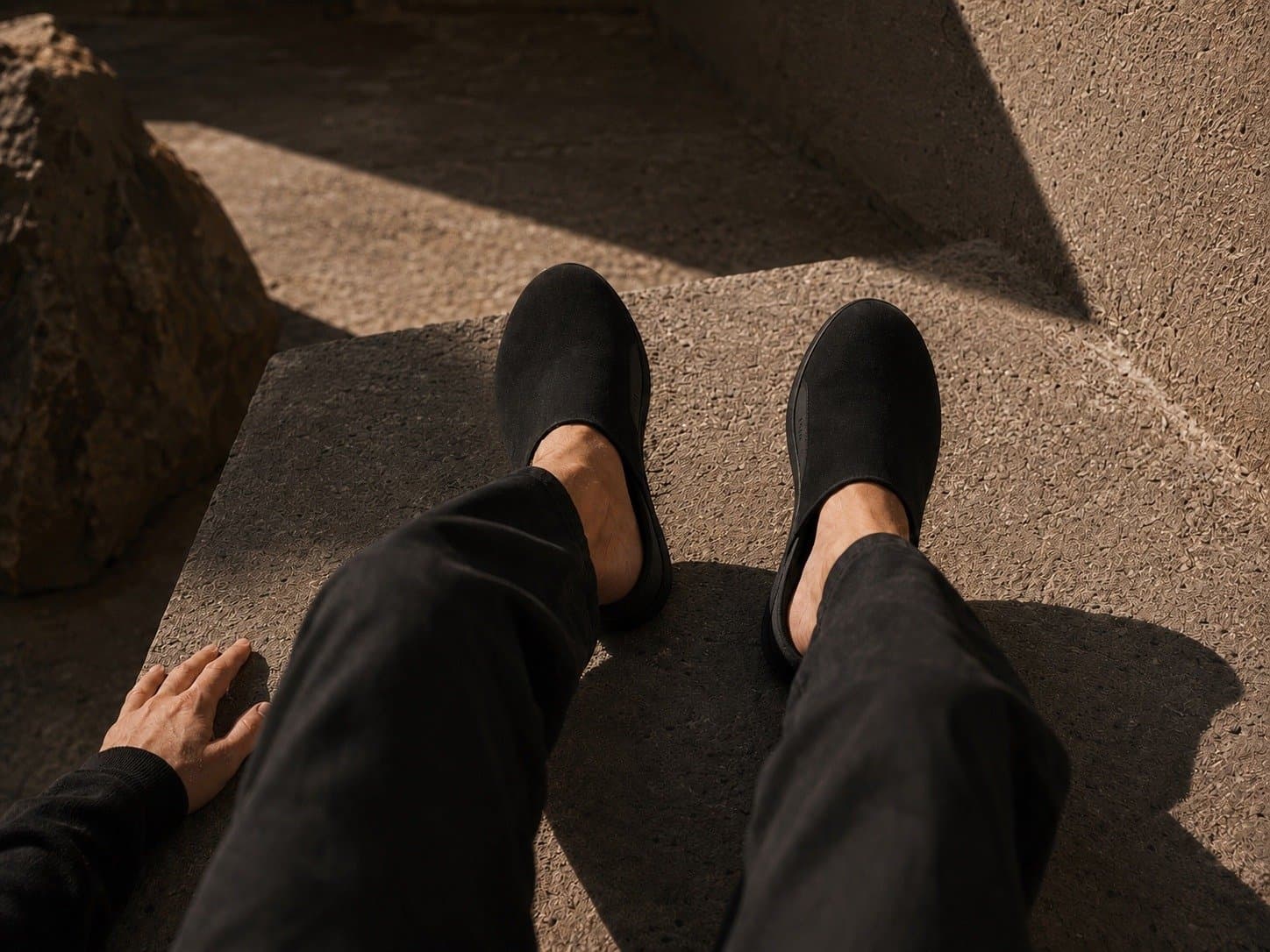Looking down at your own feet in black mules on sunlit stone.