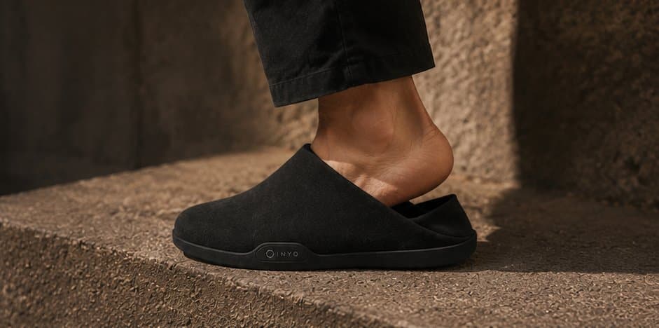 Side profile of a heel rising out of a black mule mid-step.