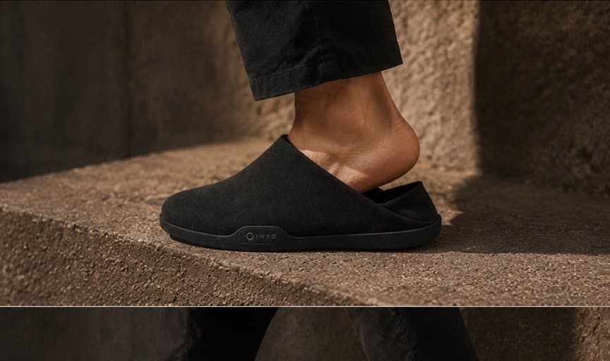 A heel pressing the collapsible panel of a black mule.